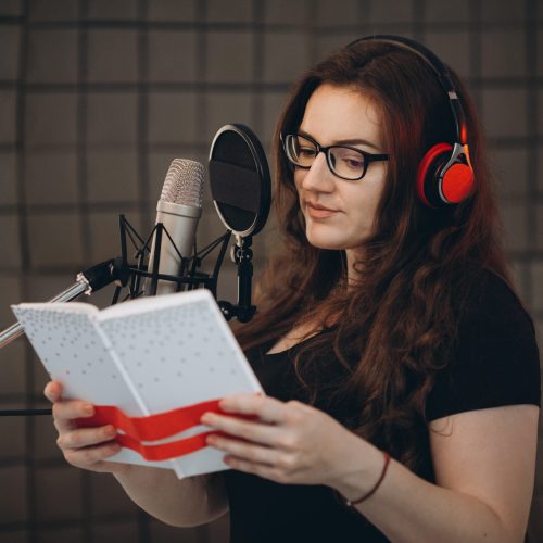 Professional female voice artist with headphones talking on mic during dubbing or voiceover. Online radio and podcasting concept.